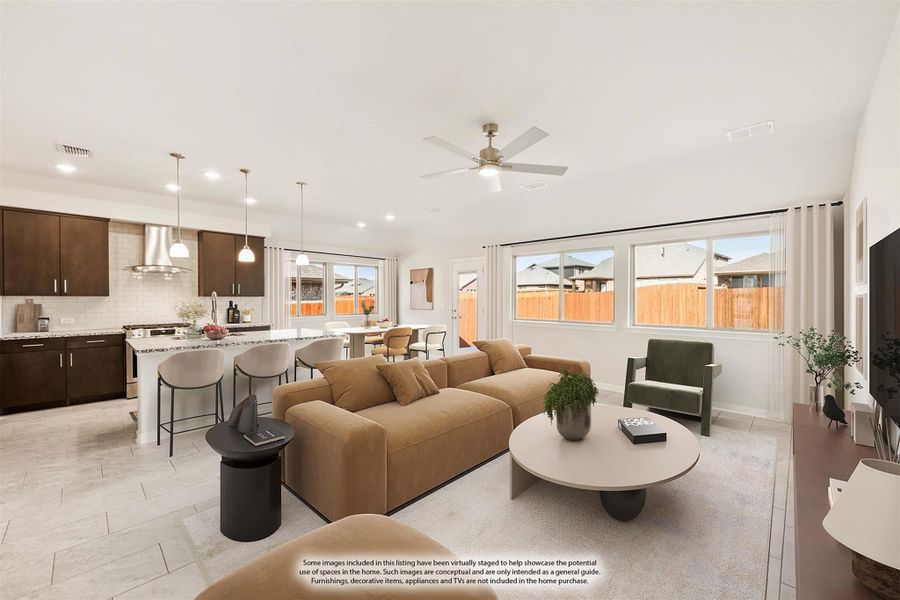 Open-concept living room with tan sofa and ceiling fan, open to kitchen with dark cabinets and island seating
