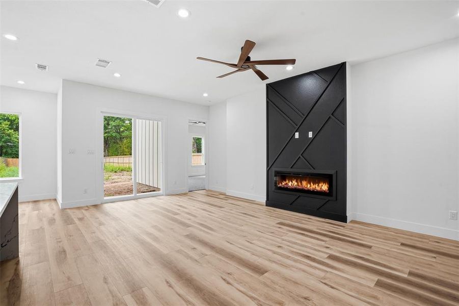 Living area featuring a modern electric fireplace with a black accent wall, wood-finish flooring, a ceiling fan, recessed lighting, and a sliding glass door to the exterior