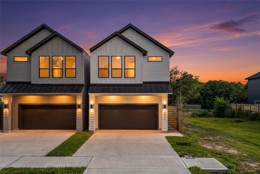 This angled twilight view shows off the modern design of the dual-unit development. Bold metal roof accents, exterior sconce lighting, and large second-story windows create an inviting, upscale look against the evening sky.