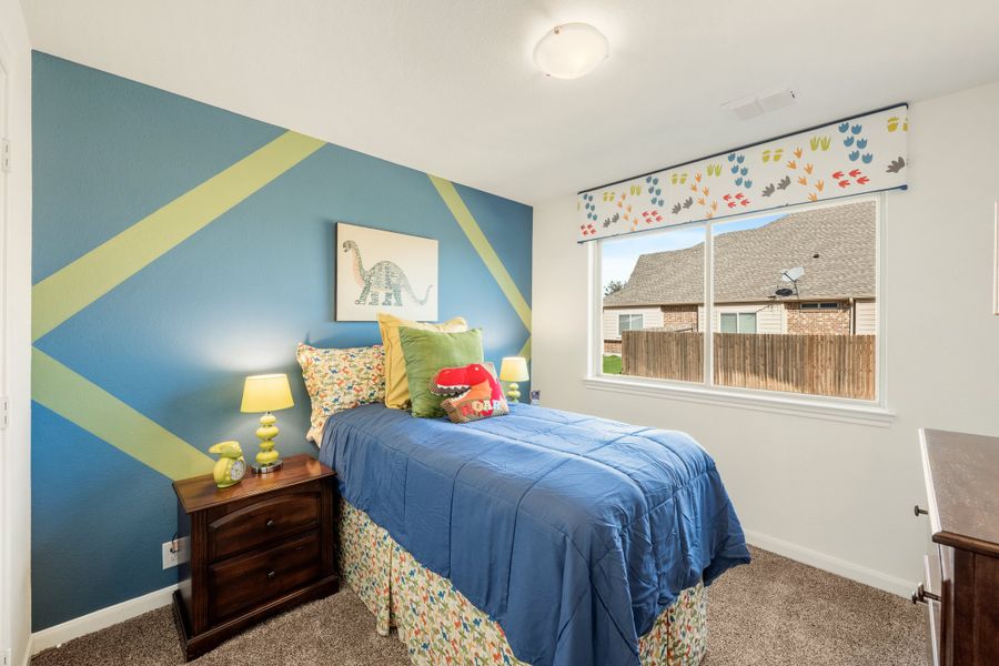 Child's bedroom with blue dinosaur-themed accent wall, twin bed, and carpet flooring