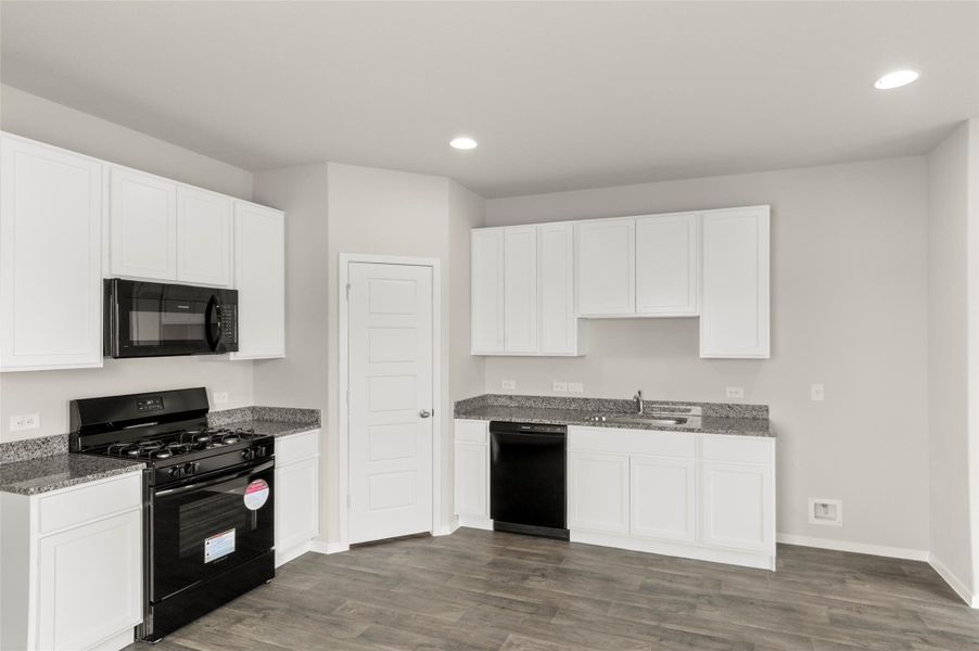 Kitchen with black appliances, white cabinetry, dark wood-style flooring, dark stone countertops, and recessed lighting