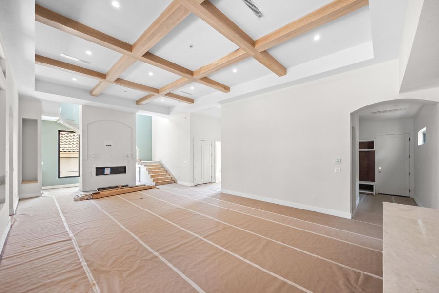 Spacious interior featuring a coffered ceiling with recessed lighting, a built-in fireplace, a large window, a staircase, and an arched entryway