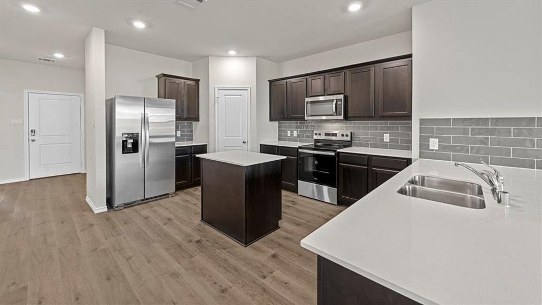 Kitchen featuring stainless steel appliances, dark wood finish cabinetry, decorative backsplash, a center island, and recessed lighting