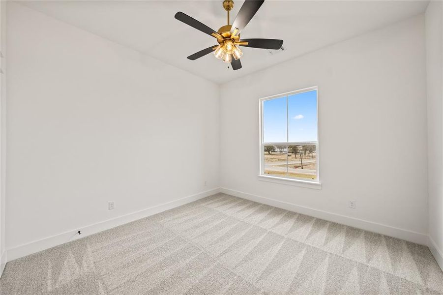 Spacious room featuring light-colored walls, patterned carpeting, a large window, and a ceiling fan with integrated lighting