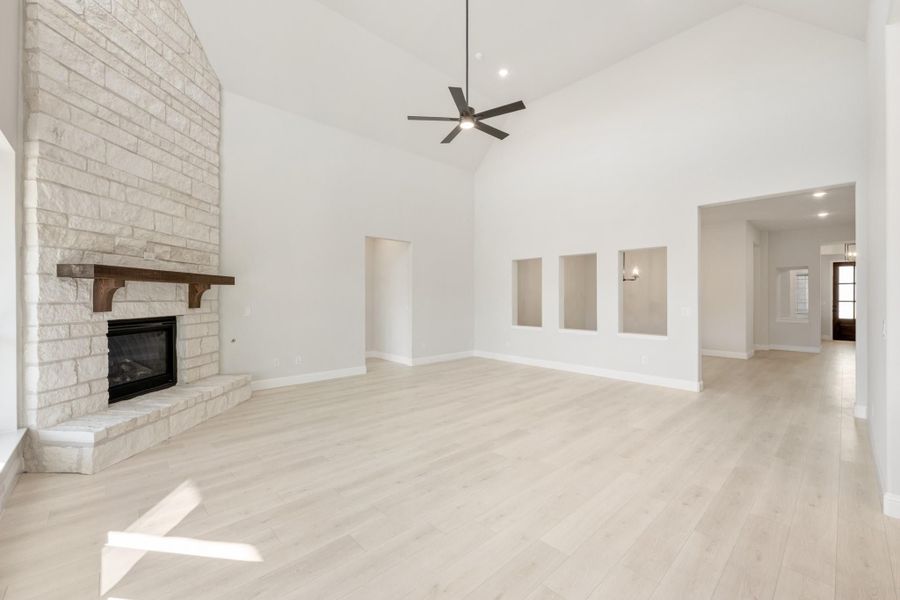 Open living room with vaulted ceiling, white brick fireplace, ceiling fan, and light hardwood floors