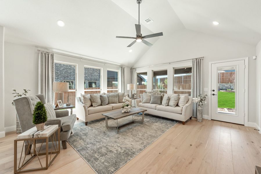 Living room with vaulted ceiling, ceiling fan, hardwood floors, two sofas, and large windows with backyard view