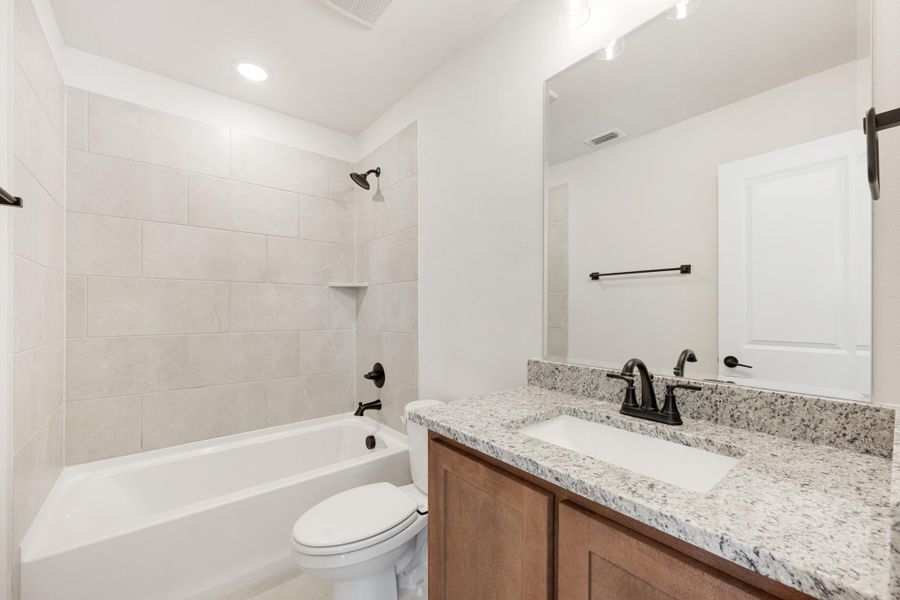 Bathroom with tiled tub-shower combo, granite vanity countertop, and dark bronze fixtures