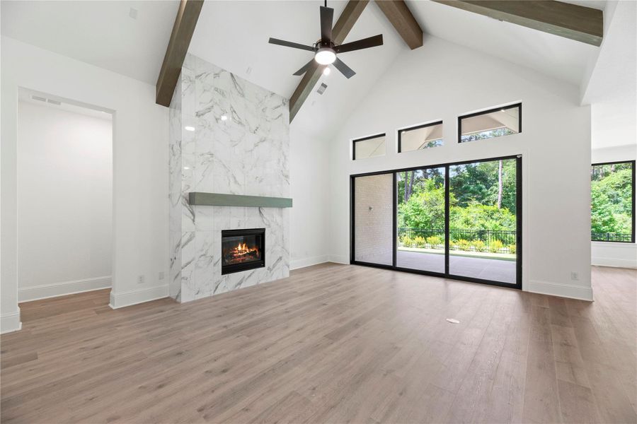 Sliding glass doors frame peaceful greenbelt views in this light-filled living area, featuring a vaulted ceiling, wood beams, and a marble fireplace.
