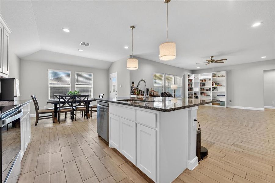 Open-concept living space featuring a kitchen island with stone countertop, wood-finish flooring, recessed lighting, built-in shelving, and vaulted ceilings