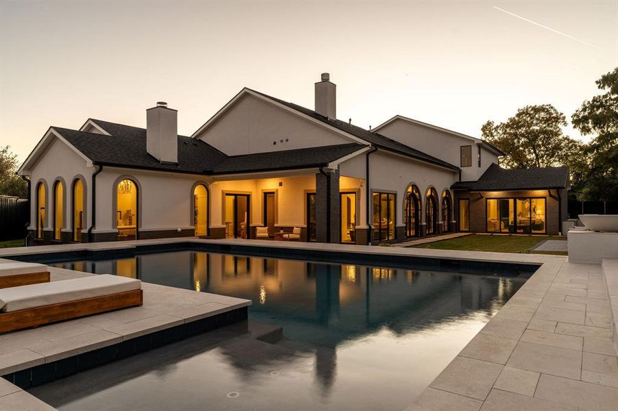 Back of property at dusk featuring a chimney, a patio, stucco siding, and an outdoor pool