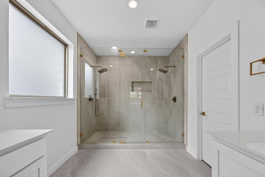 Expansive walk-in shower with dual shower heads, full-height tile, and glass enclosure with gold-tone hardware