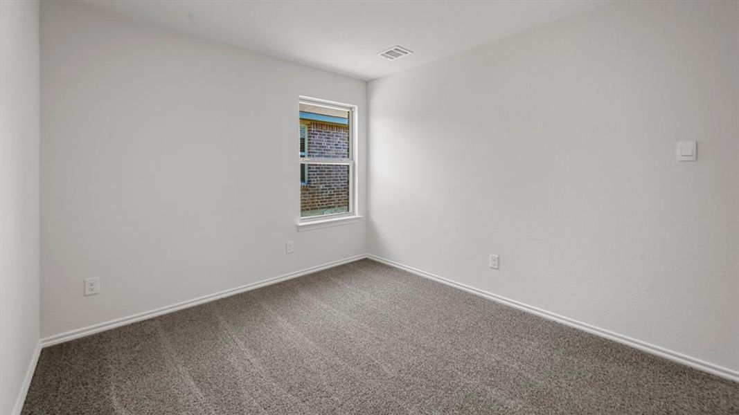 Light-filled interior space featuring neutral wall paint, gray carpeting, a window with exterior brick siding visible, and white baseboards