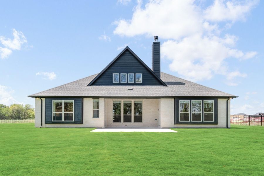 Rear exterior of single-story home with dark siding, brick, chimney, patio, and large green backyard