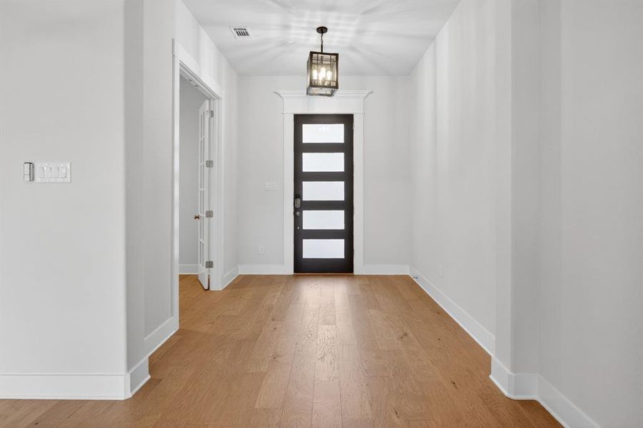 Spacious entryway featuring wood-finish flooring, a contemporary pendant light fixture, and a modern door with frosted glass panels Spacious entryway featuring wood-finish flooring, a contemporary pendant light fixture, and a modern door with frosted glass panels