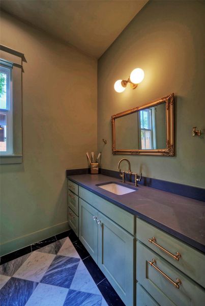 A refined powder bathroom vanity featuring rich wood cabinetry, stone countertops, and classic checkered flooring.