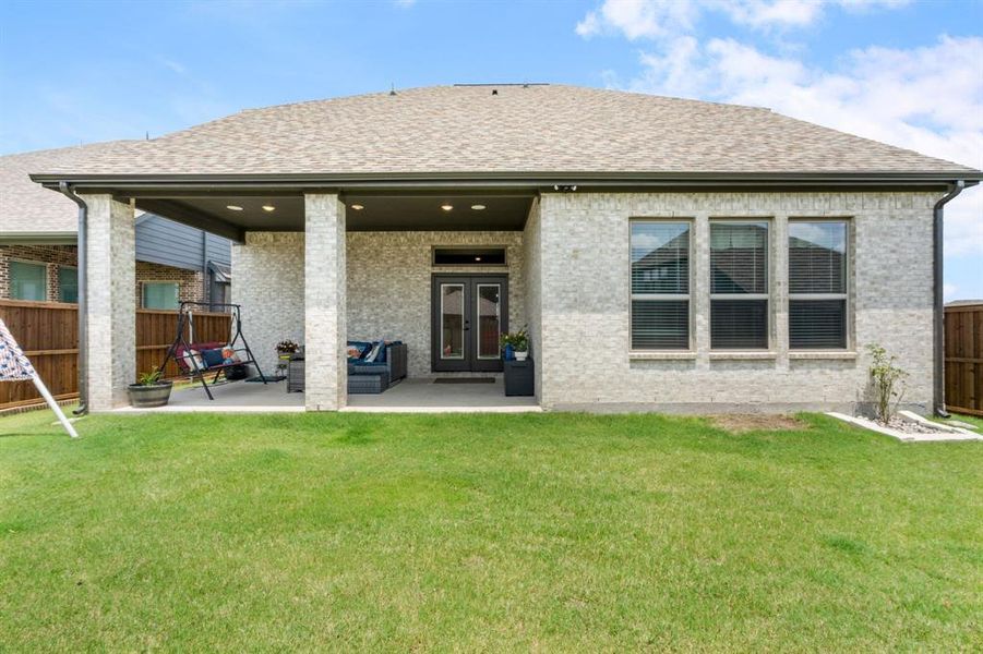 Expansive backyard featuring a covered patio with recessed lighting, brick columns, and a double-door exterior entry Expansive backyard featuring a covered patio with recessed lighting, brick columns, and a double-door exterior entry