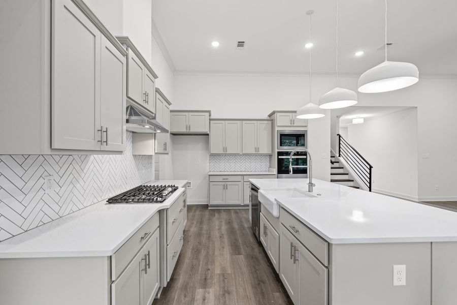 Kitchen featuring tasteful backsplash, hanging light fixtures, dark wood finished floors, an island with sink, and light stone counters