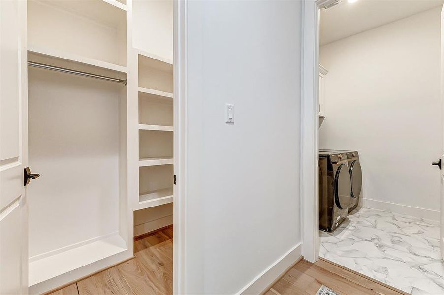 A bright upstairs laundry room with Samsung washer and dryer, adjacent to a spacious walk-in closet with ample shelving and hanging space. The area features hardwood and marble-like flooring, offering a clean and stylish look.