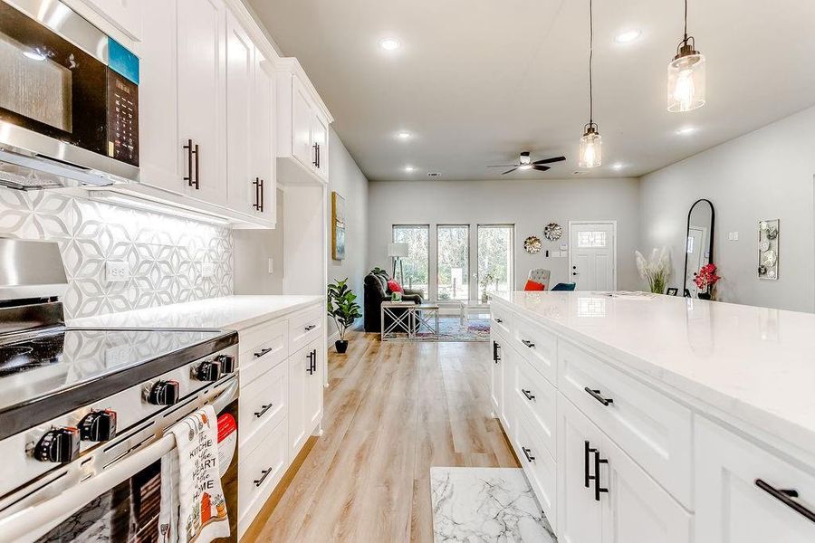 Kitchen with ceiling fan, hanging light fixtures, stove, light hardwood / wood-style floors, and white cabinets