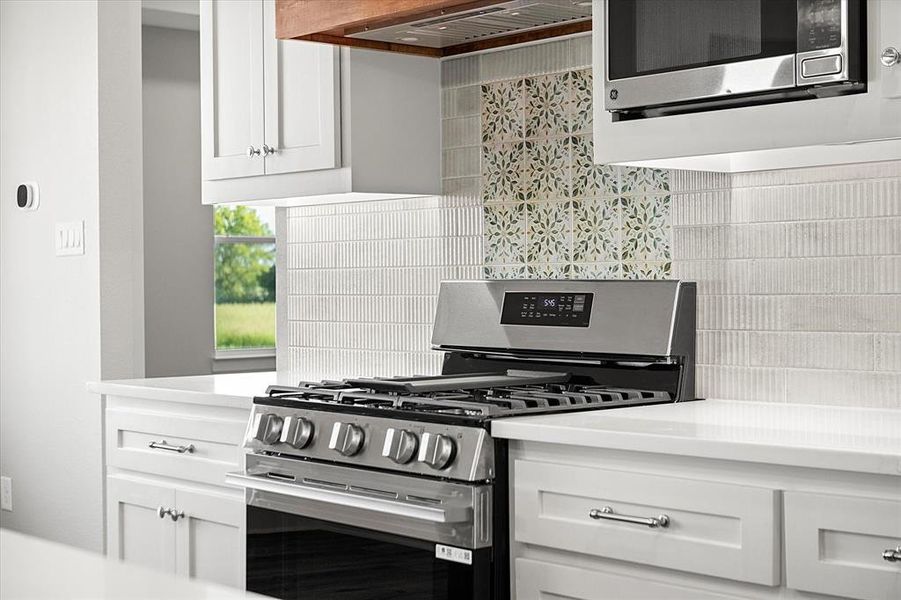 Kitchen featuring appliances with stainless steel finishes, white cabinets, tasteful backsplash, and custom exhaust hood Kitchen featuring appliances with stainless steel finishes, white cabinets, tasteful backsplash, and custom exhaust hood