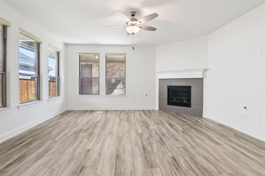 Unfurnished living room with light wood-type flooring, a tiled fireplace, and a ceiling fan Unfurnished living room with light wood-type flooring, a tiled fireplace, and a ceiling fan