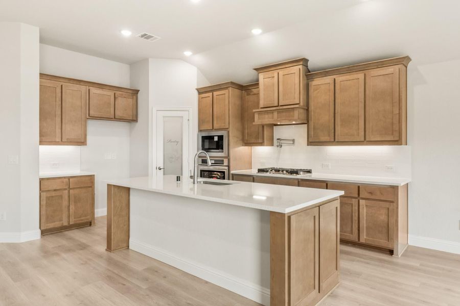 Kitchen with light wood cabinets, white countertops, center island with sink, and stainless steel appliances on light hardwood floors Kitchen with light wood cabinets, white countertops, center island with sink, and stainless steel appliances on light hardwood floors