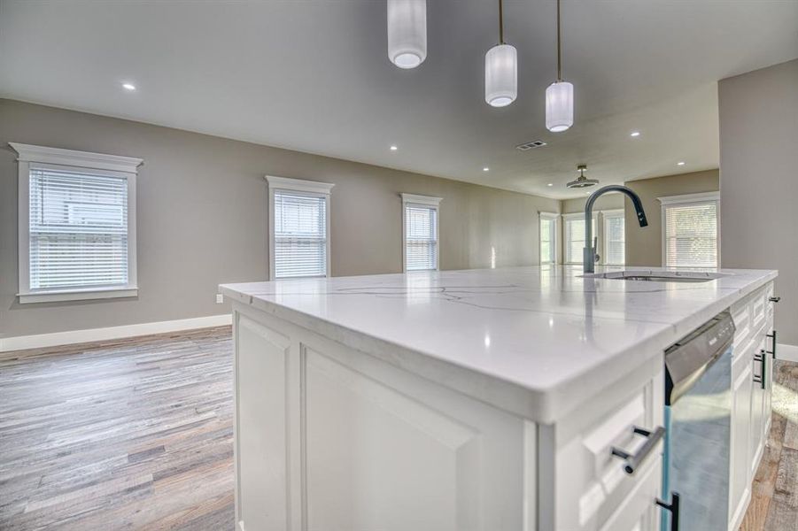 Kitchen with white cabinetry, a large island with sink, light stone counters, open floor plan, and recessed lighting