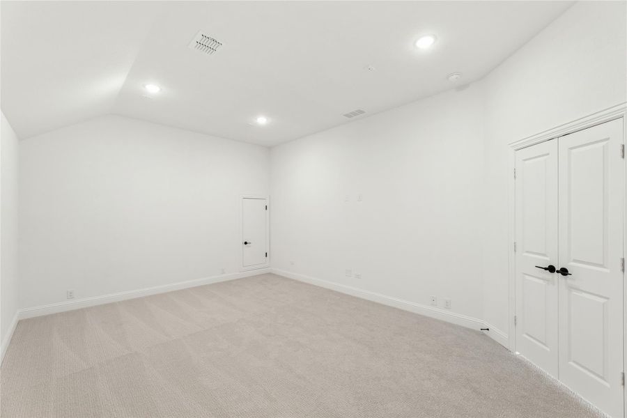Empty bedroom with vaulted ceiling, light carpet, recessed lighting, and double closet doors
