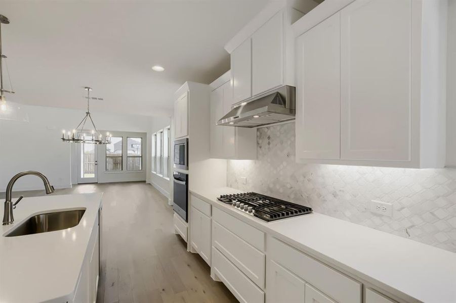 Kitchen featuring white shaker cabinetry, light-toned countertops, a stainless steel gas cooktop, built-in double ovens, and a patterned tile backsplash