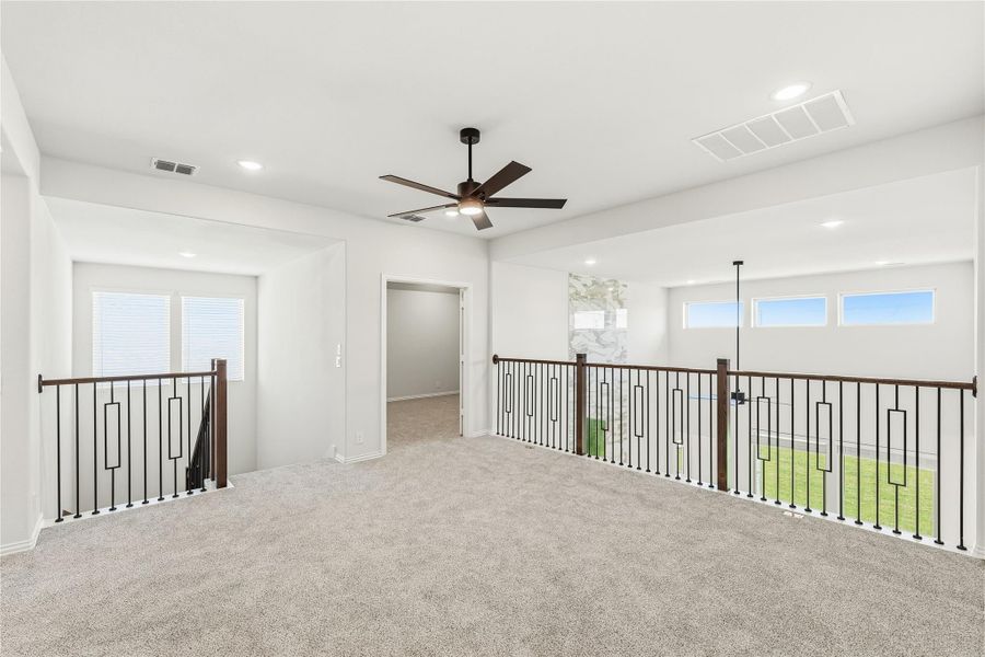 Open upstairs loft with carpet, ceiling fan, and metal stair railing overlooking lower level