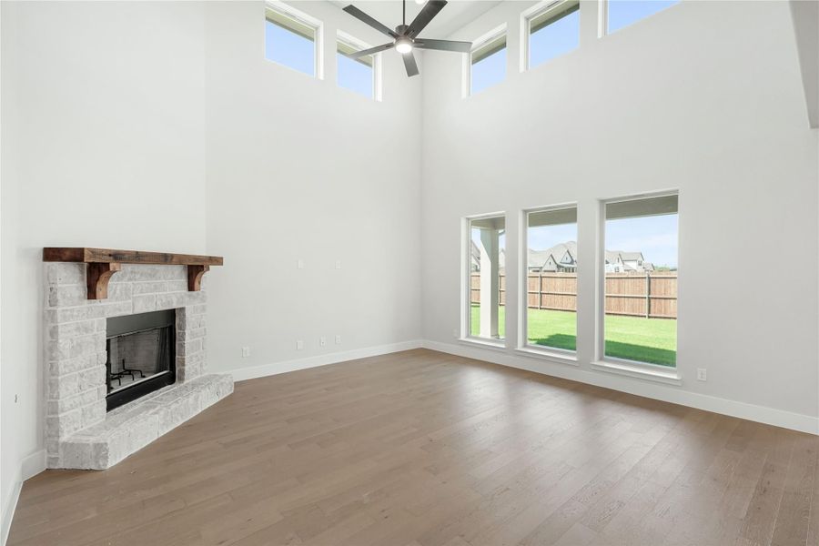 Living room with two-story ceiling, stone fireplace, hardwood floors, and large windows overlooking backyard Living room with two-story ceiling, stone fireplace, hardwood floors, and large windows overlooking backyard