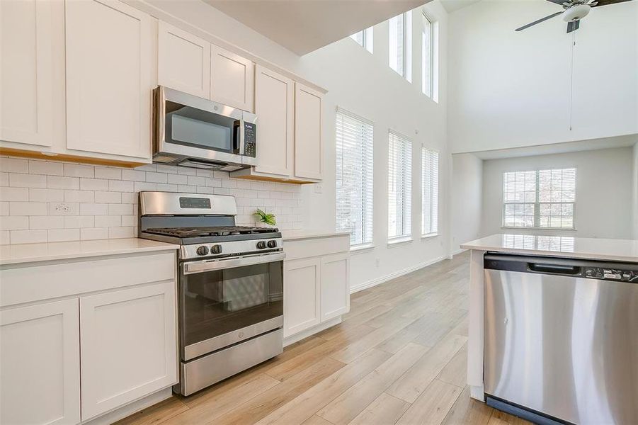 Kitchen featuring white cabinets, decorative backsplash, appliances with stainless steel finishes, and light hardwood / wood-style flooring