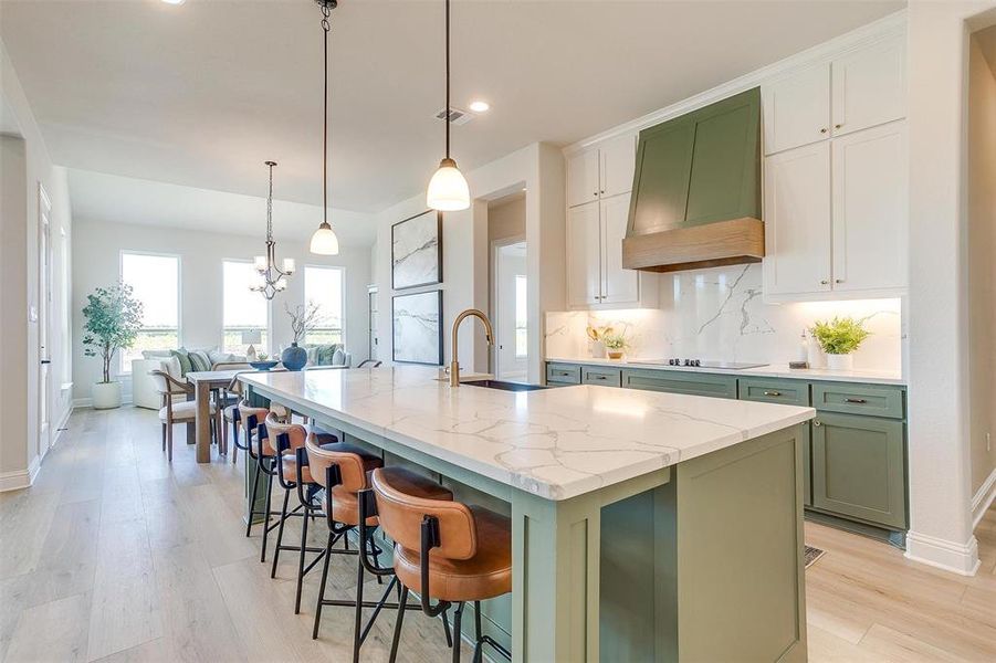 Kitchen featuring green cabinets, light stone countertops, custom exhaust hood, and a center island with sink