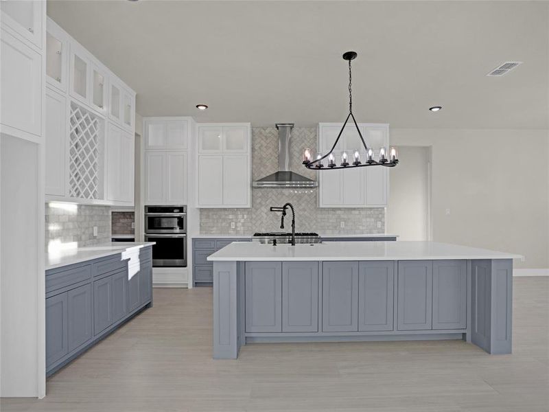 Kitchen featuring pendant lighting, a kitchen island with sink, wall chimney range hood, and white cabinets