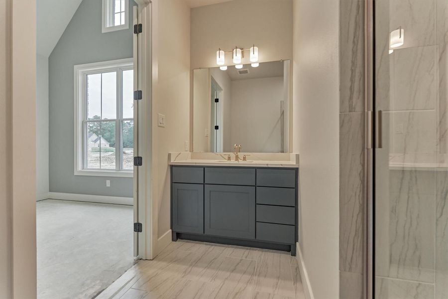 Private en-suite bath featuring a navy vanity with quartz countertops, modern lighting, and a sleek tiled shower—perfect for a comfortable suite.”