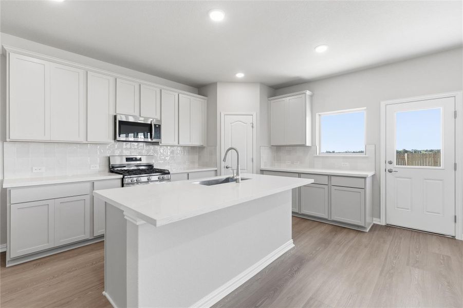 Kitchen with stainless steel appliances, tasteful backsplash, a center island with sink, light wood finished floors, and recessed lighting