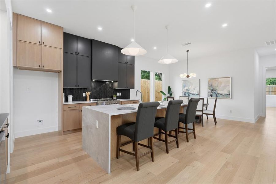 Open-concept kitchen featuring two-tone cabinetry, a waterfall island with seating, a built-in gas range, and wood-finish flooring Open-concept kitchen featuring two-tone cabinetry, a waterfall island with seating, a built-in gas range, and wood-finish flooring