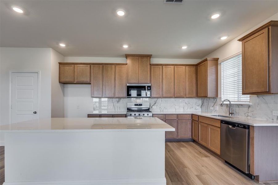 Kitchen with tasteful backsplash, light wood-type flooring, brown cabinetry, appliances with stainless steel finishes, and recessed lighting