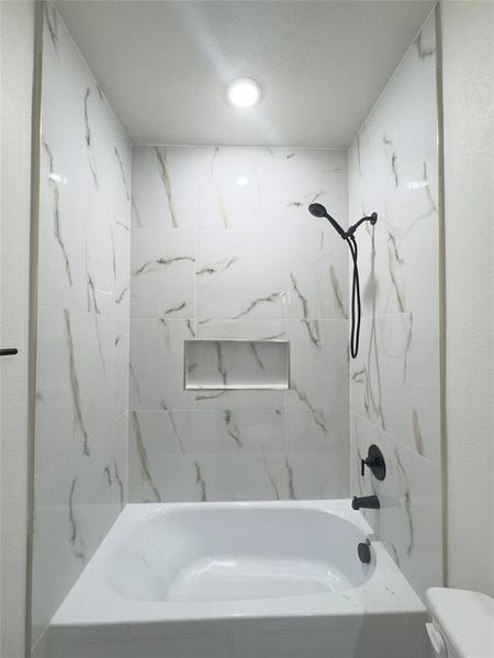 Bathroom featuring toilet, tiled shower / bath combo, and a textured ceiling