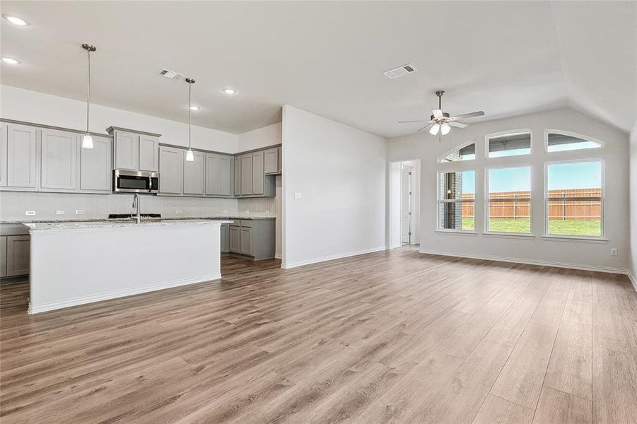 Kitchen featuring lofted ceiling, hanging light fixtures, light stone countertops, light wood-type flooring, and gray cabinets