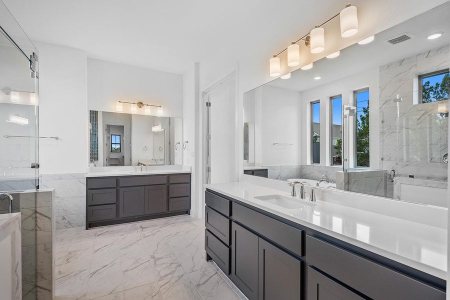 Full bathroom with a marble finish shower, light marble finish floors, and two vanities