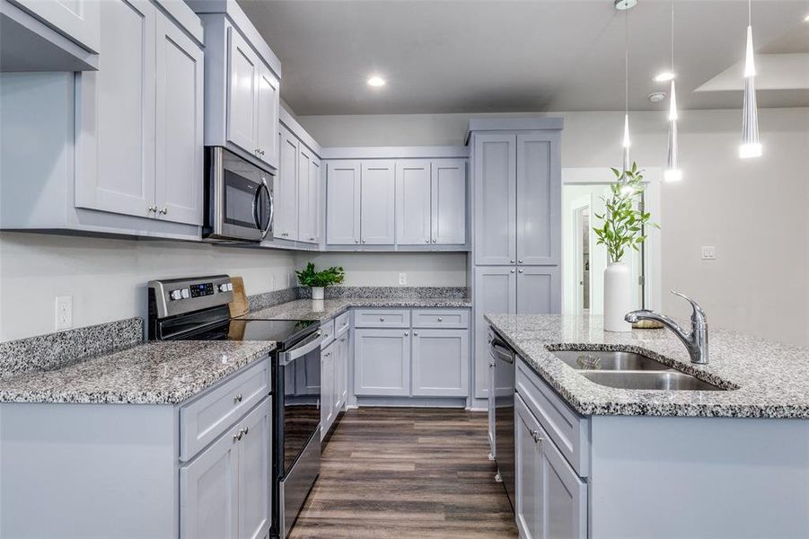 Kitchen featuring stainless steel appliances, pendant lighting, dark wood finished floors, light stone counters, and recessed lighting