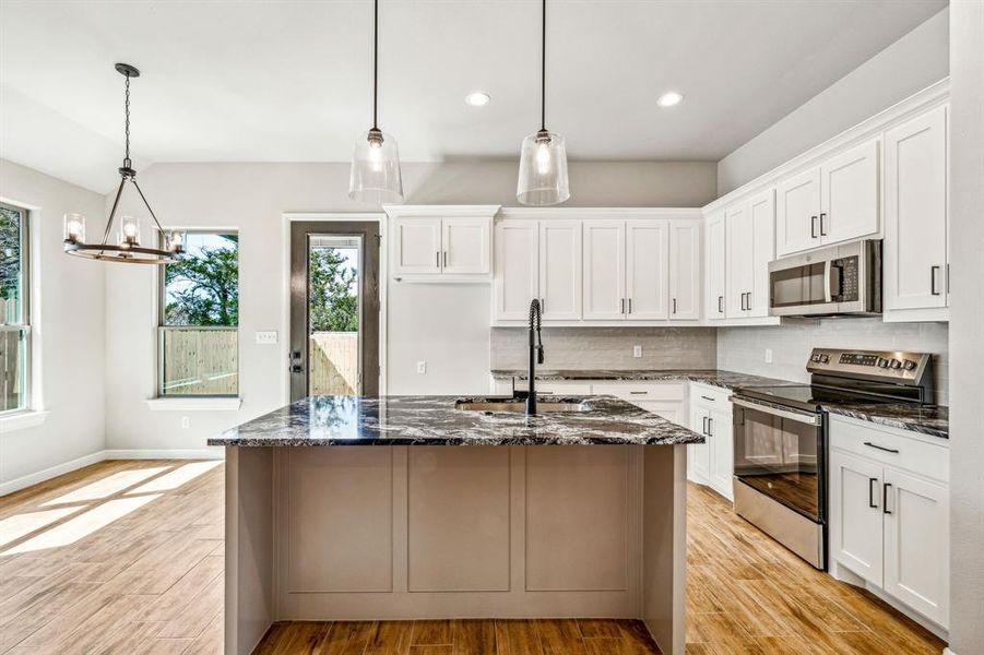 Kitchen with backsplash, stainless steel appliances, sink, dark stone countertops, and light wood-type flooring