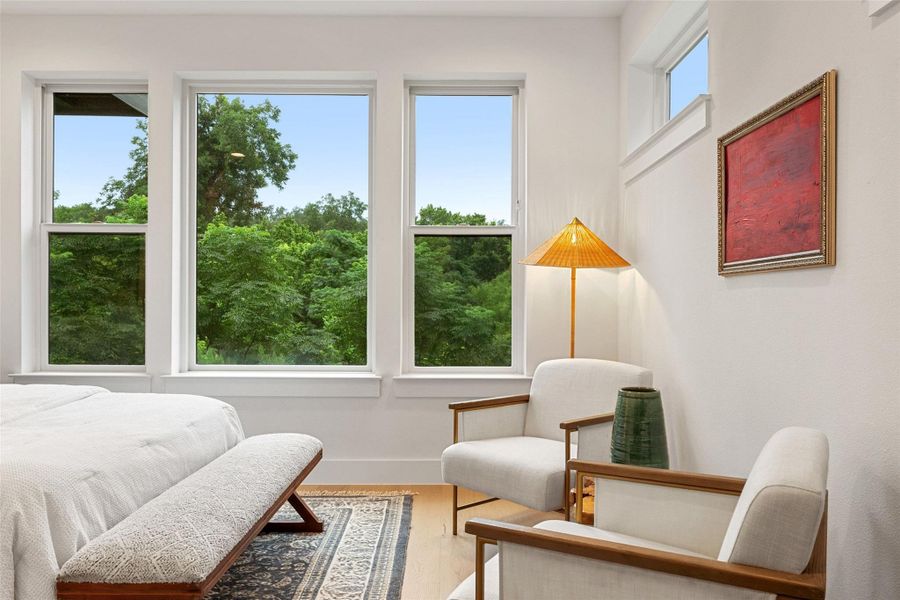A well-lit bedroom with serene tree views through expansive windows, complemented by light hardwood flooring. A well-lit bedroom with serene tree views through expansive windows, complemented by light hardwood flooring.