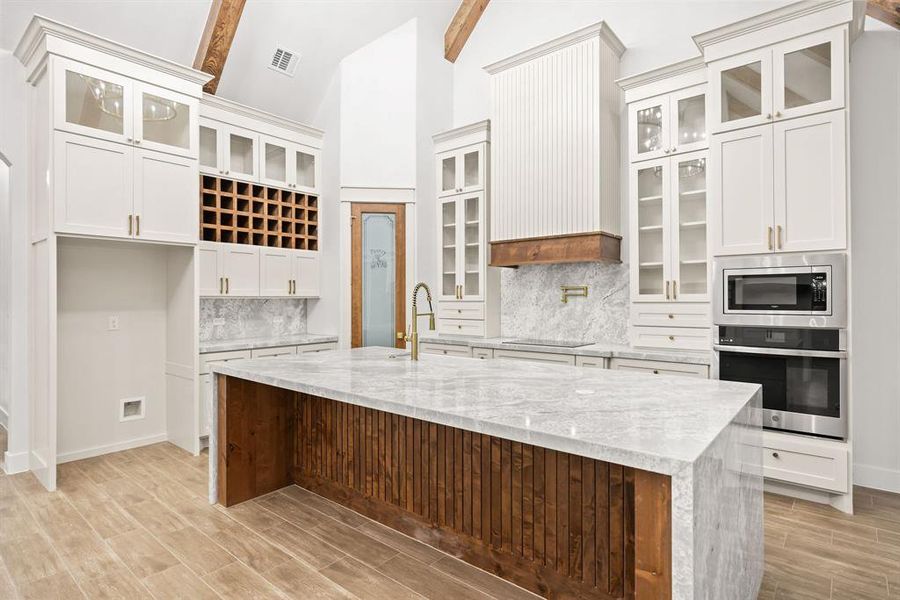 Expansive kitchen featuring a large central island with waterfall countertop, integrated wine storage, built-in stainless steel appliances, and wood-finish flooring