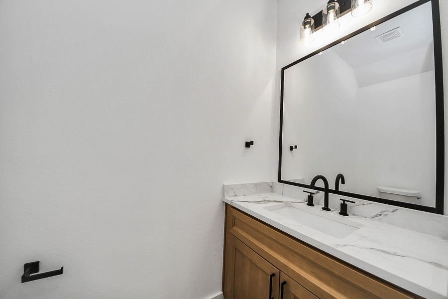Stylish first-floor half bath featuring a modern vanity with warm wood cabinetry, sleek black fixtures, and a clean quartz countertop. A perfect blend of function and design, offering a polished and convenient space for guests.