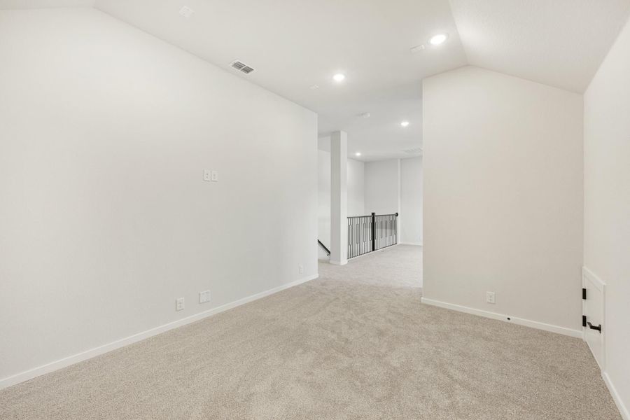 Open upstairs loft area with beige carpet, white walls, recessed lighting, and black metal stair railing visible in background.