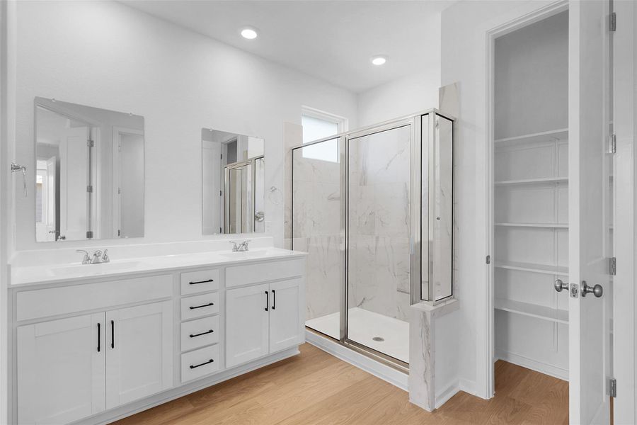 Full bath with a marble finish shower, light wood finished floors, double vanity, and a spacious closet Full bath with a marble finish shower, light wood finished floors, double vanity, and a spacious closet