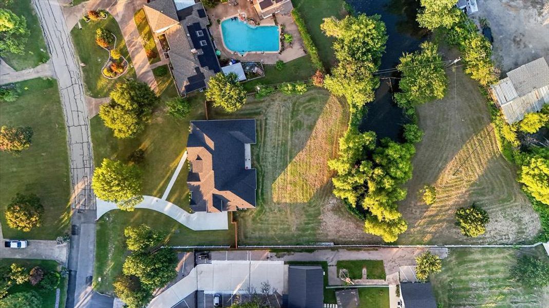 Aerial property view featuring a dark shingle roof, a curving concrete driveway, a manicured lawn, and mature trees Aerial property view featuring a dark shingle roof, a curving concrete driveway, a manicured lawn, and mature trees