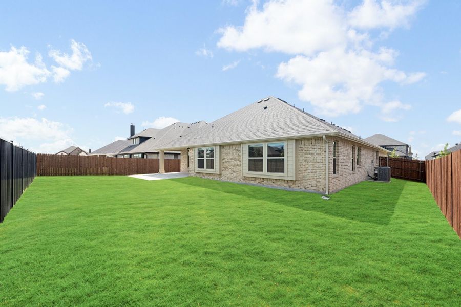 Brick home rear exterior with large grassy backyard, concrete patio, and wood privacy fence
